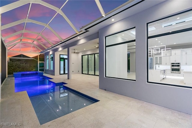 pool at dusk with glass enclosure, an in ground hot tub, sink, a patio, and ceiling fan