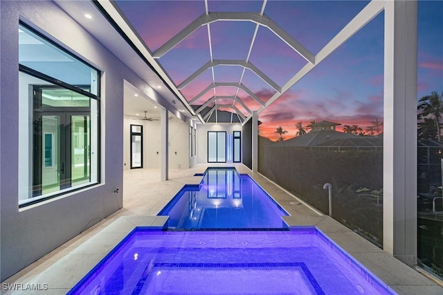 pool at dusk featuring glass enclosure, french doors, and a patio