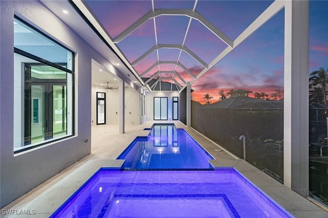 pool at dusk with an in ground hot tub, a ceiling fan, a fenced in pool, a lanai, and a patio