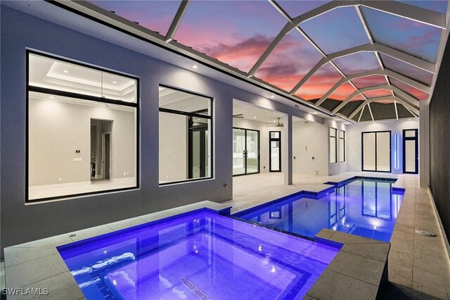 pool at dusk featuring a lanai, a patio area, and an in ground hot tub