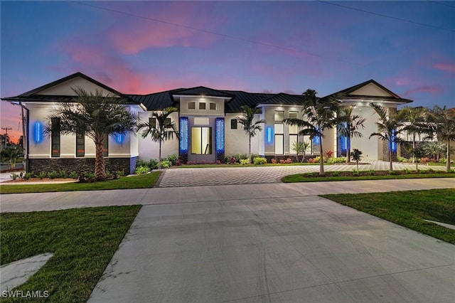 view of front facade featuring a standing seam roof, stucco siding, decorative driveway, a lawn, and metal roof