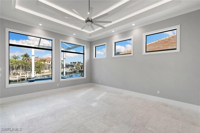 spare room with ceiling fan, plenty of natural light, a tray ceiling, and a water view