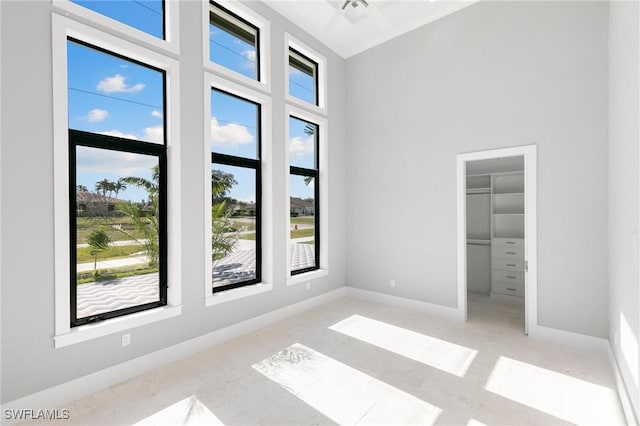 unfurnished bedroom featuring a towering ceiling, a walk in closet, baseboards, and a closet