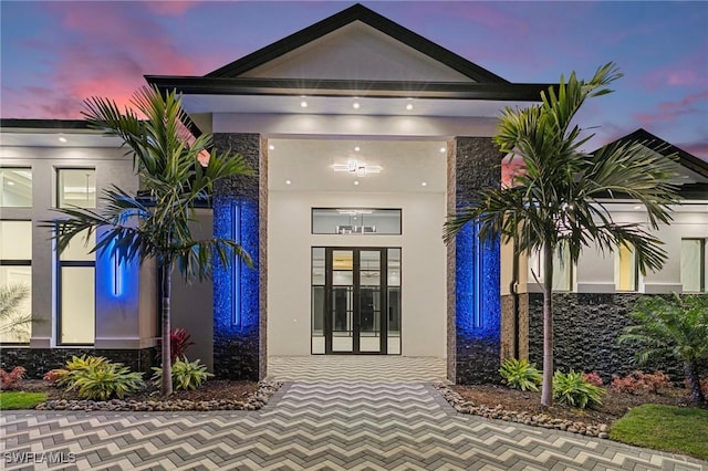 view of exterior entry with french doors, stone siding, and stucco siding