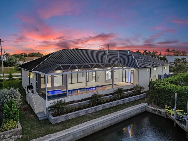 back house at dusk featuring glass enclosure, a water view, and a patio