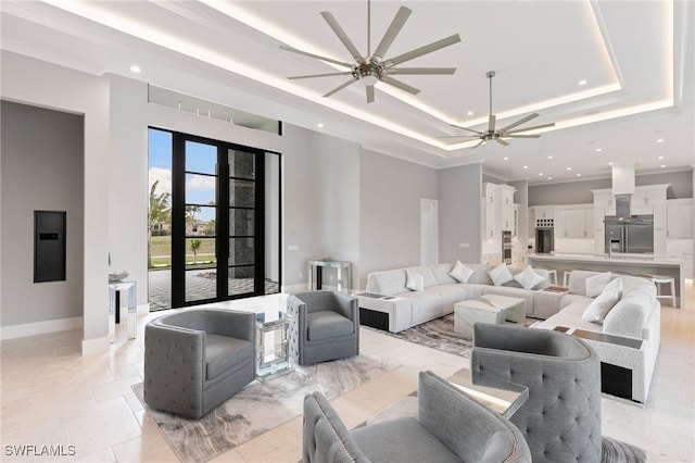 living room featuring a ceiling fan, baseboards, a tray ceiling, recessed lighting, and a towering ceiling