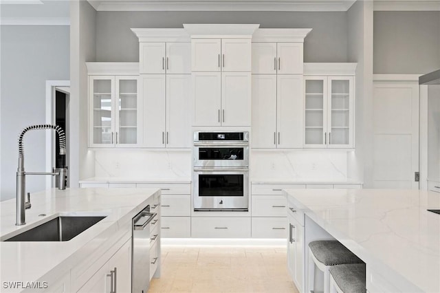 kitchen featuring white cabinetry, light stone countertops, stainless steel appliances, and a sink