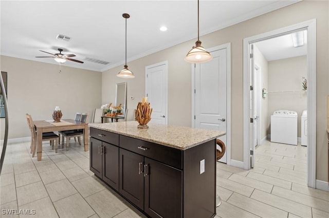 kitchen featuring washer and clothes dryer, a center island, decorative light fixtures, ceiling fan, and dark brown cabinets