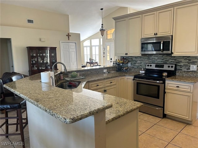 kitchen with sink, hanging light fixtures, stainless steel appliances, cream cabinets, and a kitchen bar