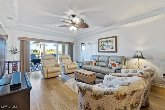 living room with a raised ceiling, crown molding, ceiling fan, and light wood-type flooring