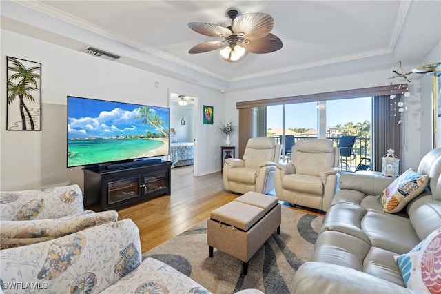 living room featuring a tray ceiling, ceiling fan, ornamental molding, and light wood-type flooring