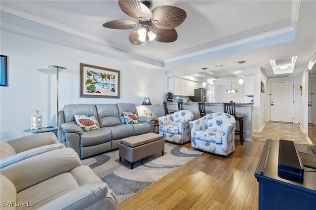 living room featuring light hardwood / wood-style floors, a raised ceiling, ceiling fan, and ornamental molding