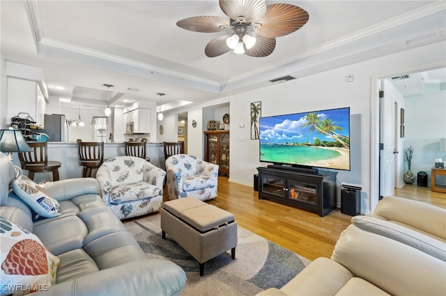 living room featuring ceiling fan with notable chandelier, light wood-type flooring, a raised ceiling, and ornamental molding