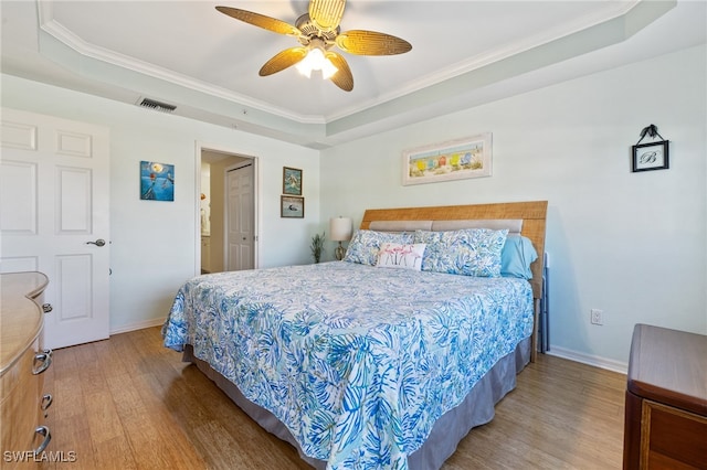 bedroom featuring a tray ceiling, ceiling fan, hardwood / wood-style floors, and ornamental molding