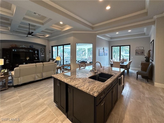 kitchen with sink, coffered ceiling, a kitchen island with sink, crown molding, and light stone countertops