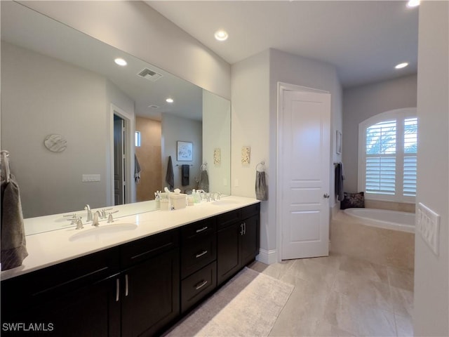 bathroom with a relaxing tiled tub, vanity, and tile patterned flooring