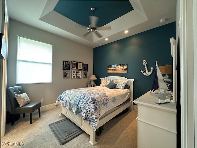 carpeted bedroom with ceiling fan and a tray ceiling