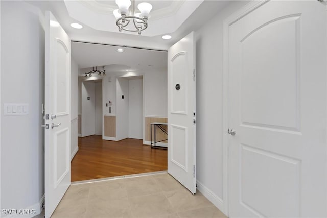 hall featuring a raised ceiling, light tile patterned flooring, crown molding, an inviting chandelier, and elevator