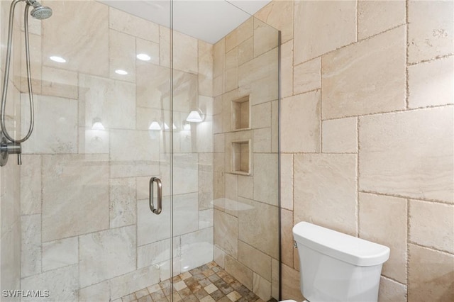 bathroom featuring a shower with door and toilet