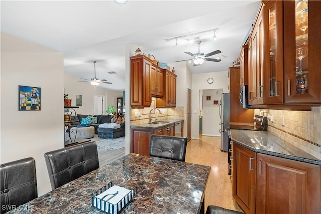 kitchen with sink, dark stone countertops, light wood-type flooring, appliances with stainless steel finishes, and tasteful backsplash