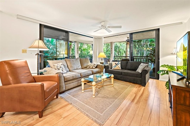 living area with a wall of windows, ceiling fan, and light wood-style flooring