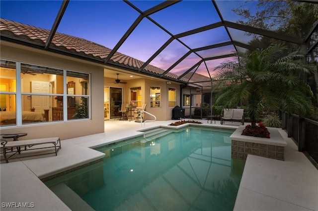 pool at dusk featuring a lanai, ceiling fan, and a patio