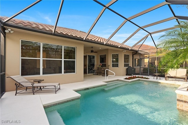 view of swimming pool featuring ceiling fan, glass enclosure, area for grilling, and a patio