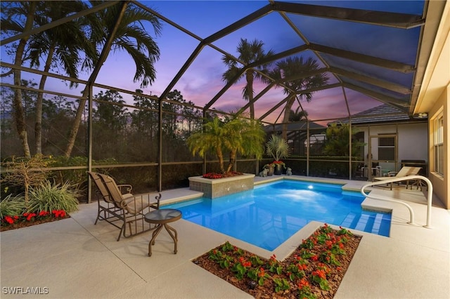 pool at dusk with glass enclosure and a patio