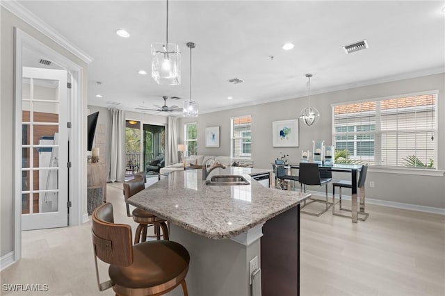 kitchen featuring plenty of natural light, a kitchen island with sink, hanging light fixtures, crown molding, and sink