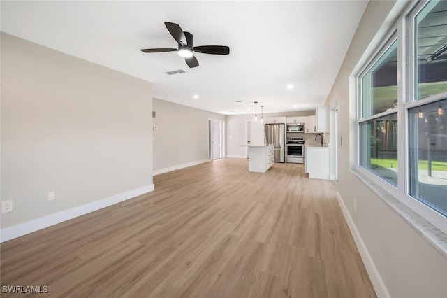 unfurnished living room featuring ceiling fan, sink, and light wood-type flooring