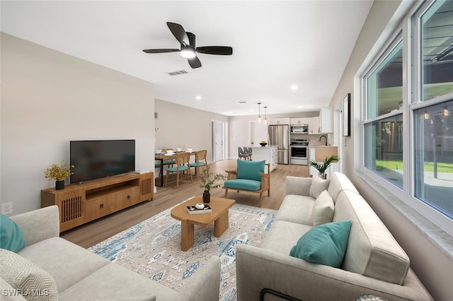 living room with ceiling fan, sink, and light wood-type flooring