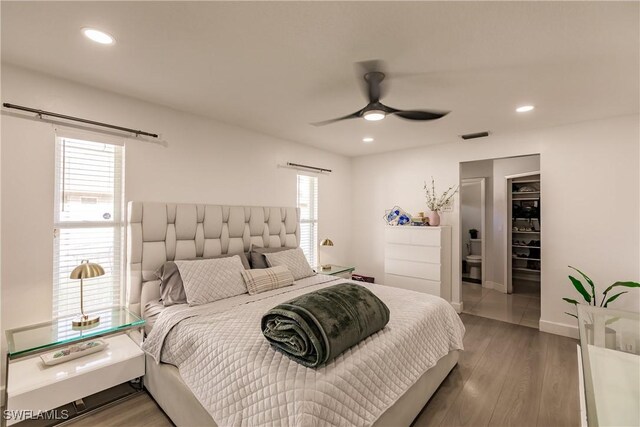 bedroom with ceiling fan, a walk in closet, hardwood / wood-style floors, and multiple windows