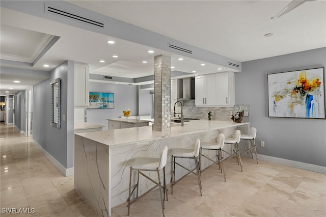 kitchen with a breakfast bar, light stone counters, white cabinets, kitchen peninsula, and wall chimney exhaust hood