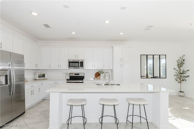 kitchen with a center island with sink, sink, ornamental molding, appliances with stainless steel finishes, and white cabinetry