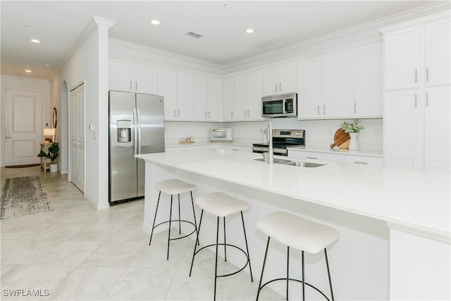 kitchen featuring white cabinetry, crown molding, a breakfast bar area, light tile patterned floors, and appliances with stainless steel finishes