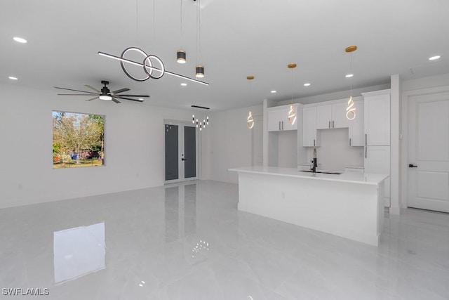 kitchen featuring pendant lighting, a center island with sink, sink, ceiling fan, and white cabinetry