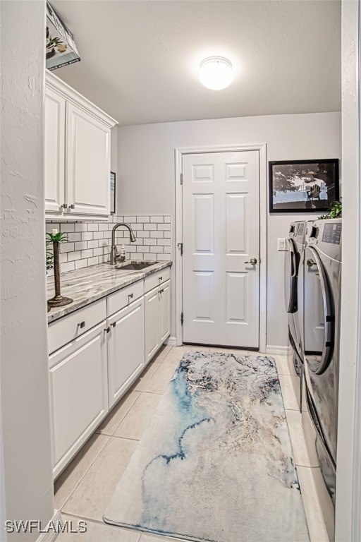 clothes washing area featuring washer and clothes dryer, sink, light tile patterned floors, and cabinets