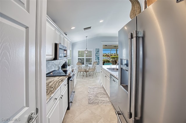 kitchen with pendant lighting, white cabinets, appliances with stainless steel finishes, lofted ceiling, and backsplash