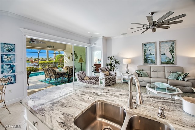 kitchen with sink, white cabinetry, ornamental molding, light tile patterned floors, and light stone counters