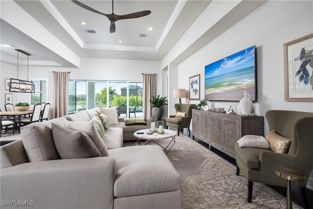 living room with ornamental molding, a tray ceiling, and ceiling fan with notable chandelier