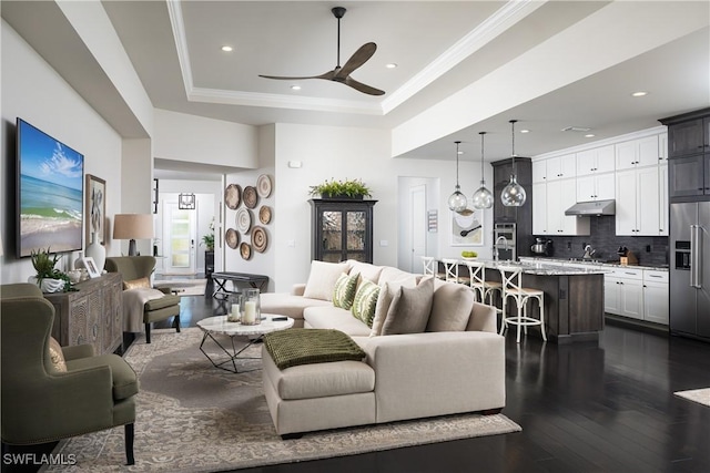 living room featuring dark hardwood / wood-style floors, ceiling fan, ornamental molding, and a tray ceiling