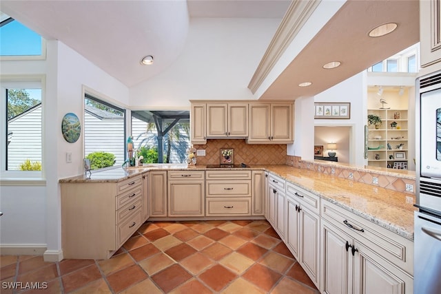 kitchen featuring tasteful backsplash, black electric stovetop, light stone counters, kitchen peninsula, and cream cabinetry