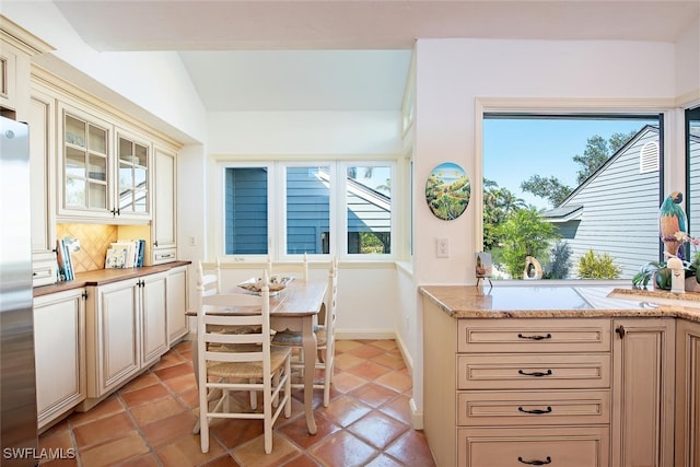 kitchen with light tile patterned floors, stainless steel fridge, light stone countertops, vaulted ceiling, and cream cabinetry