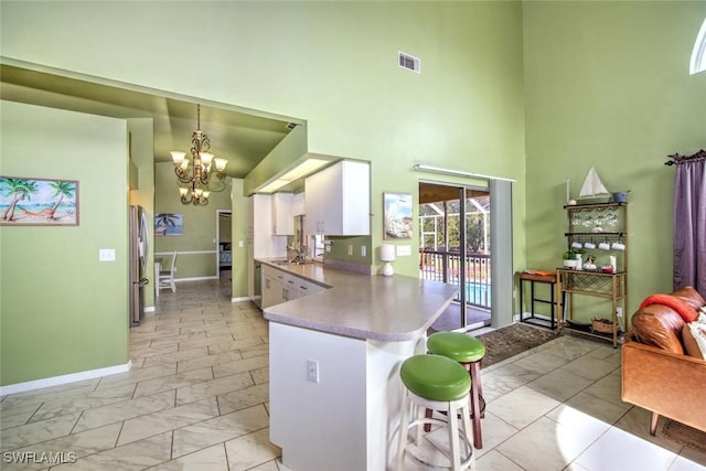 kitchen featuring a towering ceiling, stainless steel refrigerator, white cabinetry, sink, and kitchen peninsula