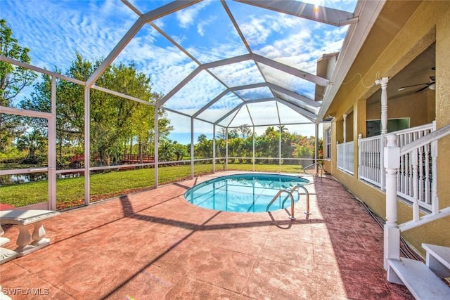 view of swimming pool with a yard, a patio area, ceiling fan, and glass enclosure