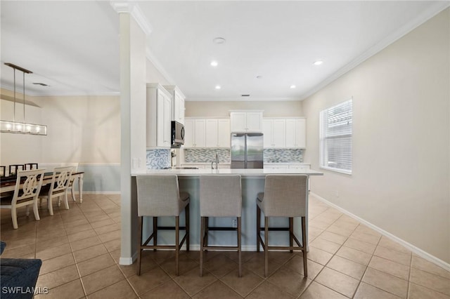 kitchen with pendant lighting, a breakfast bar area, stainless steel refrigerator, tasteful backsplash, and white cabinets