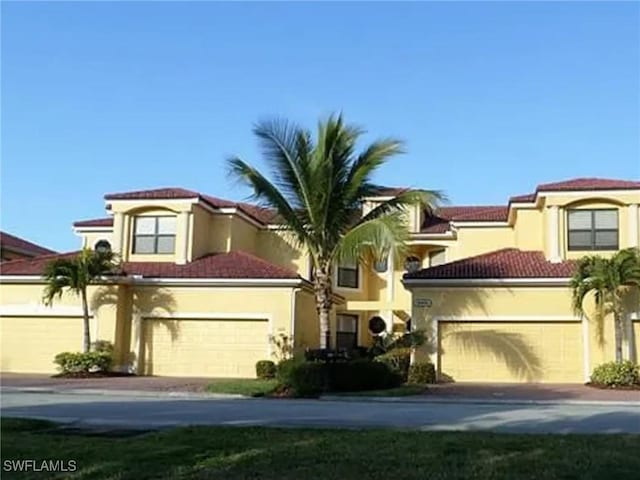mediterranean / spanish house with concrete driveway, a garage, stucco siding, and a tiled roof