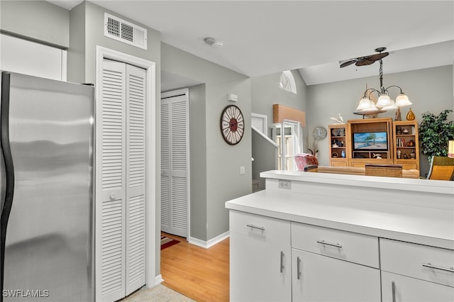 kitchen with a chandelier, stainless steel fridge, white cabinets, and pendant lighting