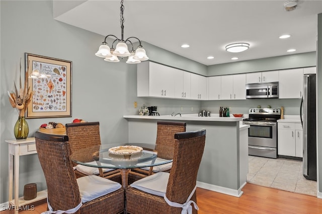 kitchen with white cabinetry, stainless steel appliances, a notable chandelier, kitchen peninsula, and pendant lighting