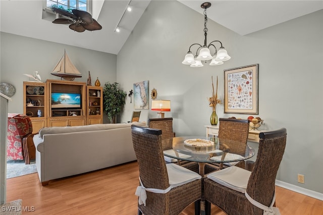 dining space featuring light hardwood / wood-style flooring, high vaulted ceiling, and ceiling fan with notable chandelier